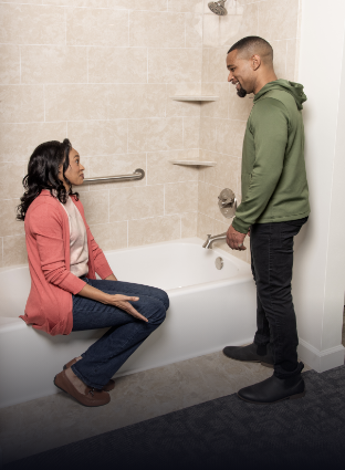 woman sitting on the side of the tub discussing a bathroom remodel with her husband in the rome bath remodeling showroom